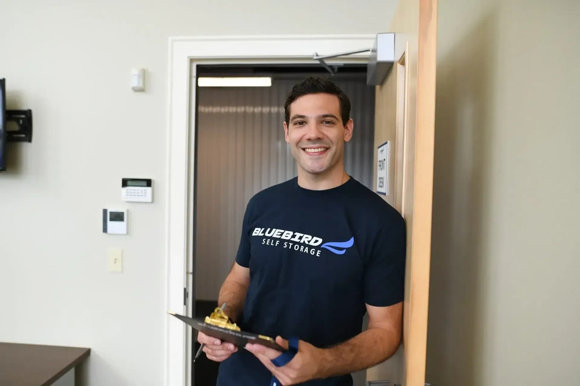 Staff member holding clipboard at Bluebird Self Storage front desk.
